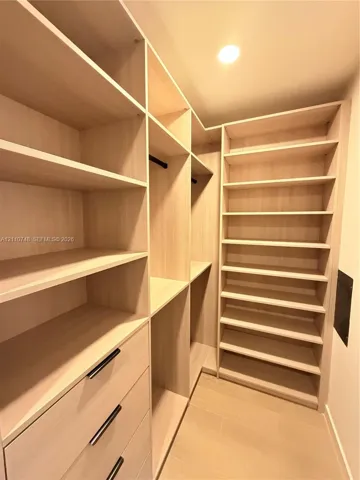 Custom walk-in storage featuring light wood-finish shelving, integrated hanging rods, multi-tier cabinetry, and minimalist matte black hardware