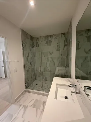 Walk-in shower with floor-to-ceiling tile, frameless glass enclosure, and wall-mounted shower head, paired with a white countertop vanity featuring an integrated rectangular sink and chrome hardware