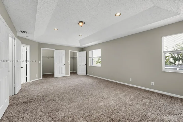 Spacious interior featuring a tray ceiling, recessed lighting, wall-to-wall carpeting, and two built-in closet spaces with six-panel doors