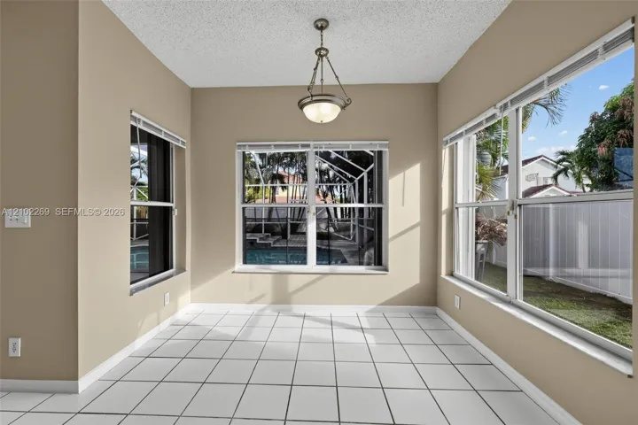 Sun-drenched room featuring large multi-pane windows, neutral tile flooring, and a central pendant light fixture