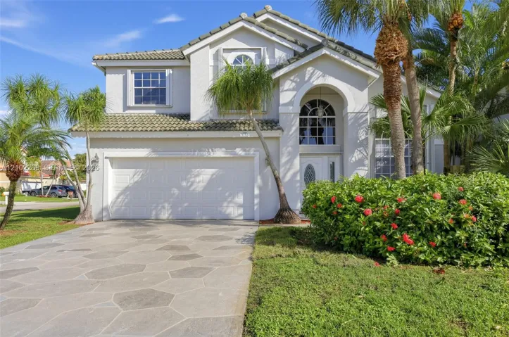 Two-story stucco exterior featuring a concrete tile roof, arched entryway with decorative glass door, multi-paned windows, and a geometric-patterned concrete driveway