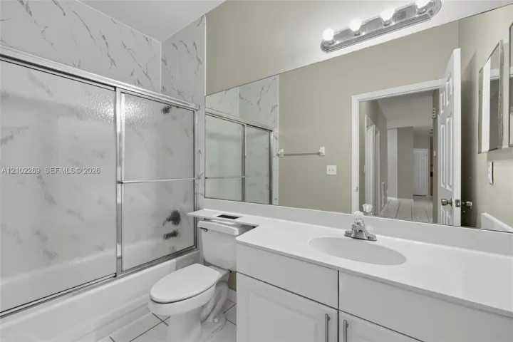 Bathroom featuring a white vanity with a solid surface countertop, an integrated oval sink, a full-width wall mirror, and a tub-shower combination with patterned wall surround and sliding glass doors