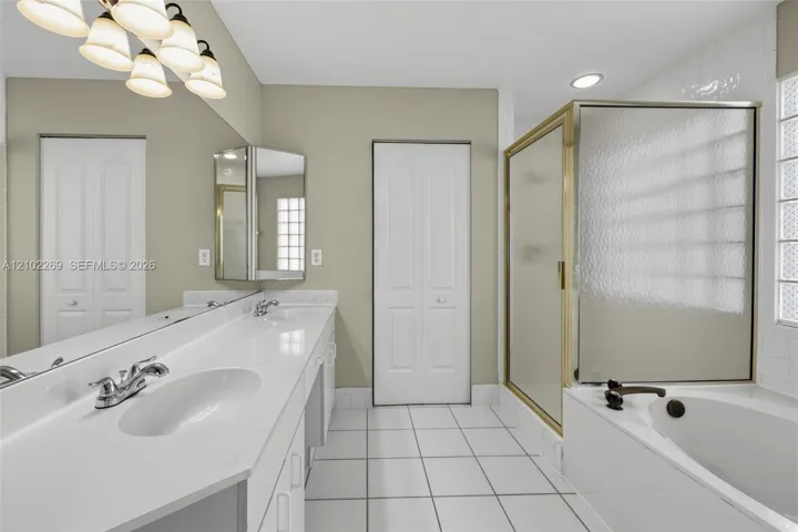 Double vanity with white solid surface countertop, glass-enclosed shower, soaking tub, and glass block window detailing