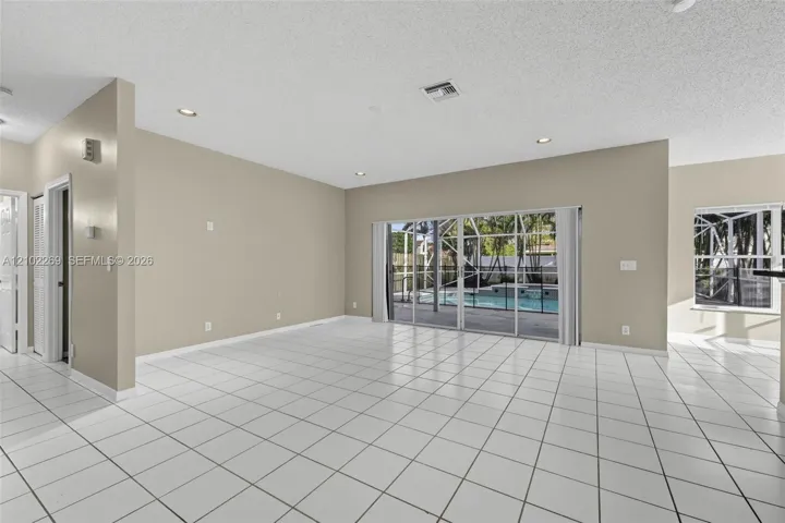 Neutral-toned interior featuring ceramic tile flooring, recessed lighting, and large sliding glass doors providing visibility to a screened-in pool area