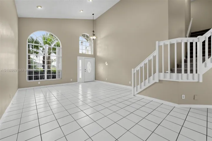 Vaulted ceiling with recessed lighting, large arched windows, tile flooring, and a white wooden staircase featuring a matching balustrade