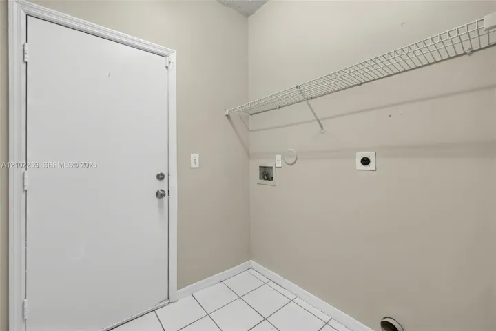 Utility area featuring white ceramic tile flooring, a solid core door, and wall-mounted wire shelving