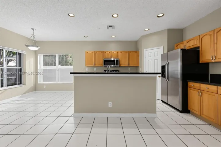 Kitchen featuring wood cabinetry, dark countertops, tile flooring, recessed lighting, and stainless steel refrigerator