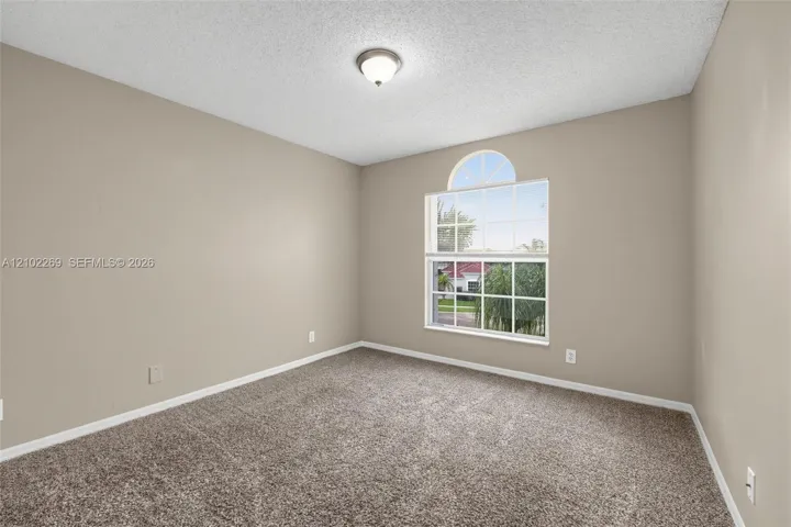 Interior space featuring neutral wall paint, wall-to-wall carpeting, an arched window with a grid pattern, and a central ceiling-mounted light fixture