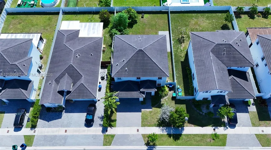 Aerial perspective of suburban properties featuring multi-level dwellings, tile roofing, paved driveways, and fenced rear grounds