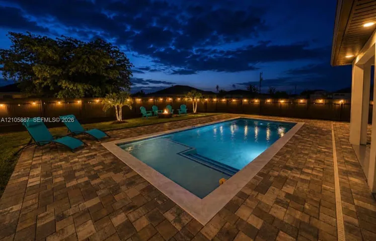Backyard featuring a concrete-paved patio, rectangular in-ground pool with integrated entry steps, manicured lawn, and perimeter privacy fencing