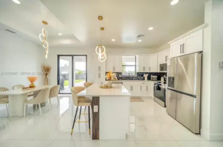 Kitchen featuring white shaker-style cabinetry, quartz countertops, central island, stainless steel appliances, and large-format tile flooring