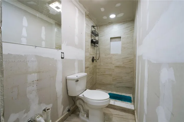 Full bathroom featuring a walk-in shower with tile surround and integrated wall niche, porcelain toilet, and wall-mounted vanity mirror