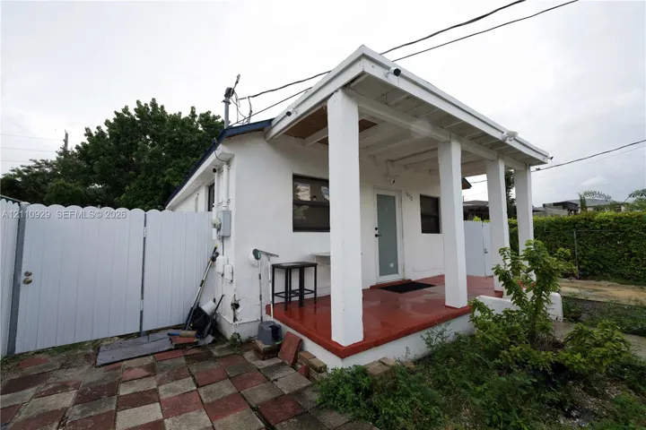 White stucco exterior featuring a covered front porch with squared columns, a paved patio area, and a white privacy gate