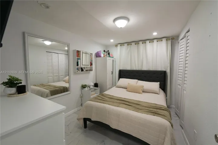 Large wall-mounted mirror, white tile flooring, louvered closet doors, and recessed lighting