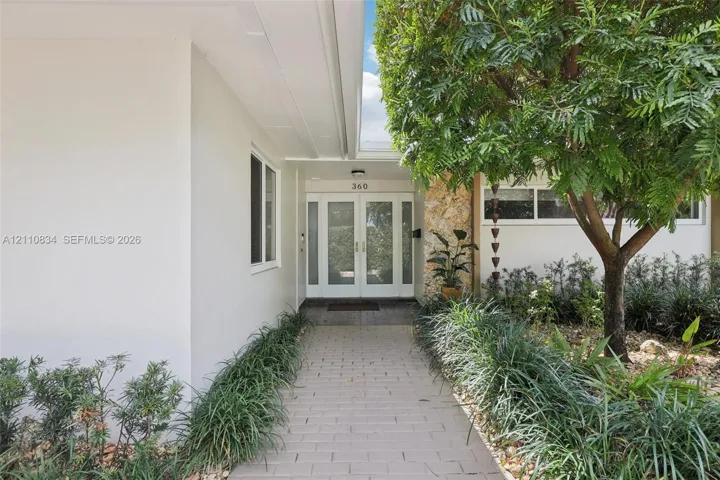 Covered entrance featuring double glass-paneled doors, stone-accented exterior wall, and paver walkway