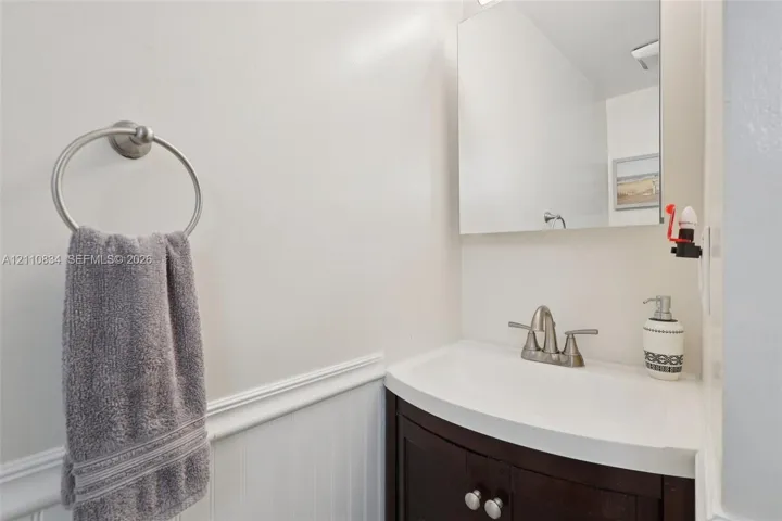 Dark wood-finish vanity with integrated sink, brushed nickel faucet, wall-mounted mirror, and white wainscoting