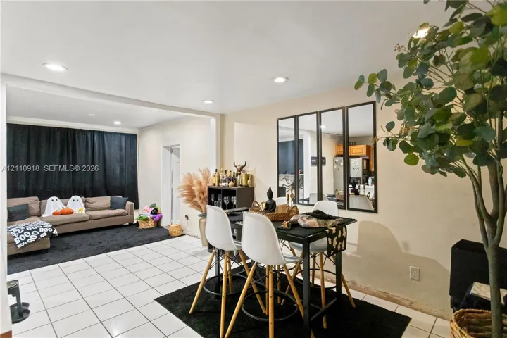 Open-concept interior featuring light-toned tile flooring, recessed ceiling lighting, and a multi-pane decorative wall mirror