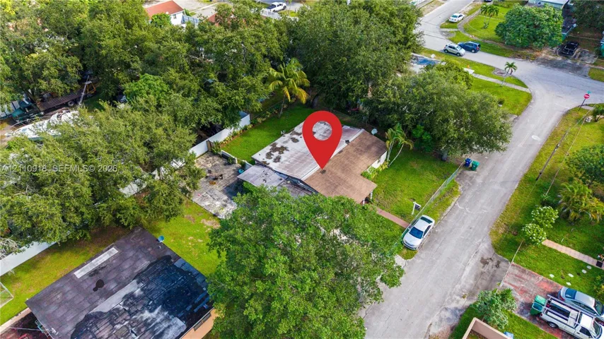 Aerial perspective featuring a shingled roof, paved driveway, expansive lawn, and mature trees