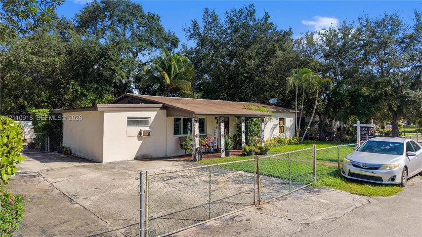 Single-story exterior featuring a concrete driveway, metal chain-link fencing, and a covered entryway