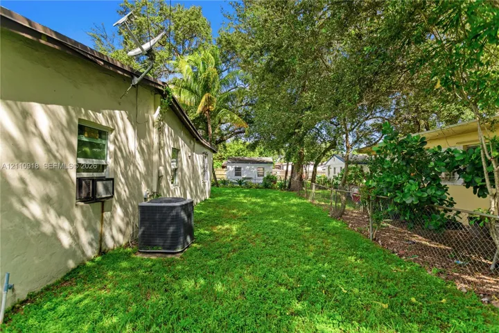 Side yard featuring a grass lawn, chain-link perimeter fencing, and mature trees