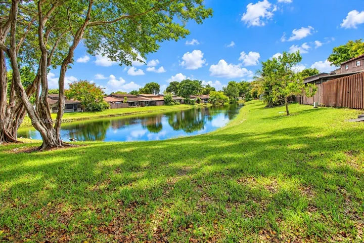 Waterfront property featuring a landscaped lawn, mature trees, and a wooden privacy fence