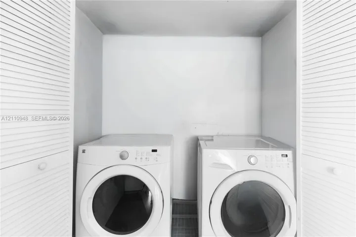Laundry area featuring white front-load appliances and dual louvered-style closet doors