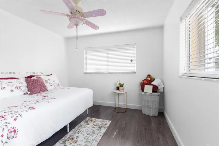 Neutral-toned interior featuring wood-finish flooring, dual windows with horizontal blinds, and a ceiling-mounted light fixture