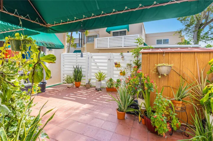 Enclosed courtyard featuring terracotta tile flooring, white horizontal slat fencing, a retractable fabric awning, and a wooden storage structure