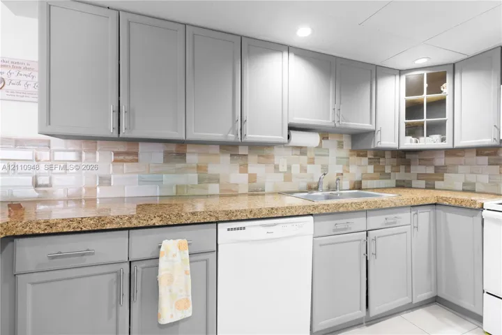 Kitchen featuring gray shaker-style cabinetry, multi-tonal subway tile backsplash, stone-surface countertops, and an undermount double-basin sink