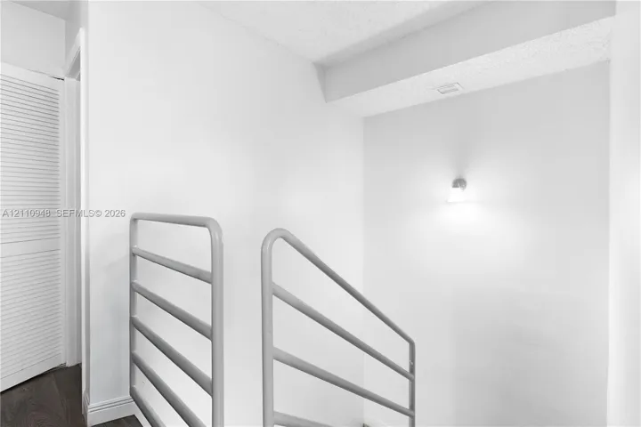 Horizontal metal stair railing, neutral wall finish, and wall-mounted light fixture