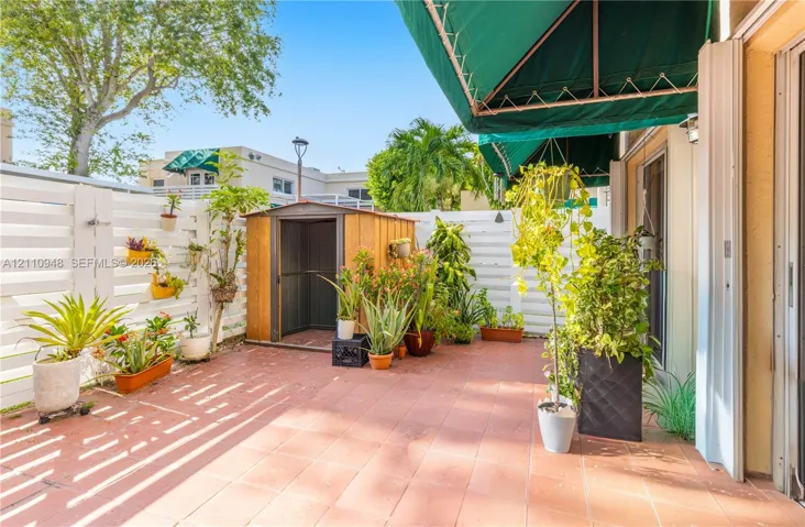 Private patio featuring terracotta tile flooring, white horizontal privacy fencing, a retractable fabric awning, and an exterior storage structure