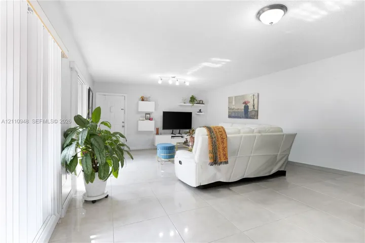 Large-format tile flooring, multi-bulb overhead track lighting, sliding glass door with vertical blinds, and floating wall-mounted shelving