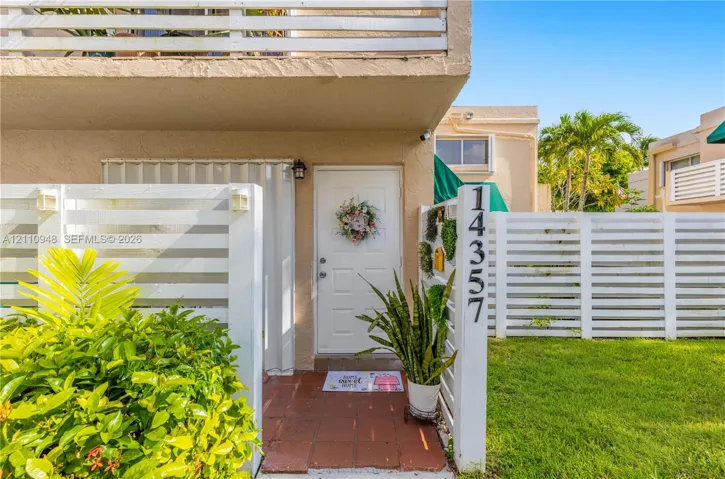 Entryway featuring a white paneled door, terracotta-toned tile flooring, and perimeter white wood-slat fencing