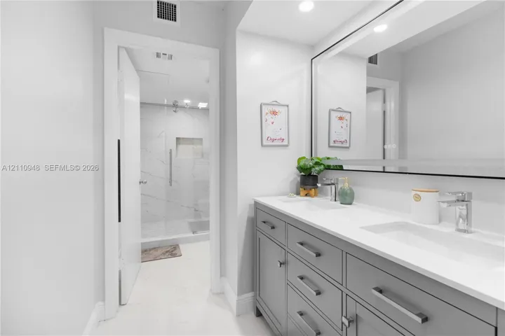 Dual-sink vanity with grey cabinetry, white solid-surface countertops, and a wide integrated mirror