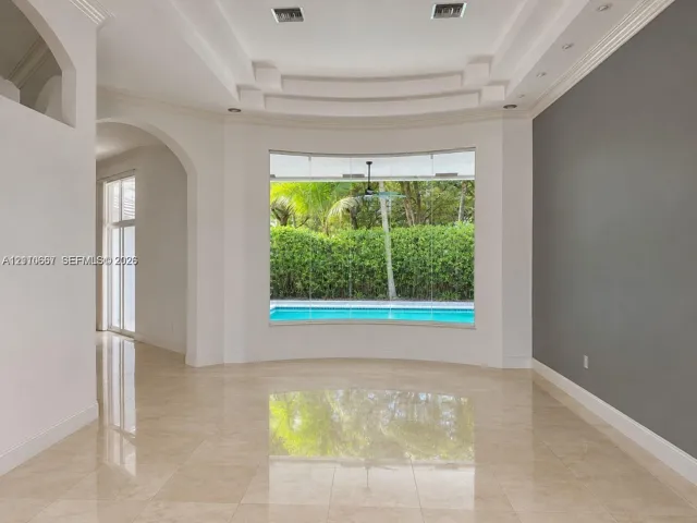 Living area featuring polished tile flooring, a recessed tray ceiling with integrated lighting, and a floor-to-ceiling picture window overlooking a swimming pool and greenery