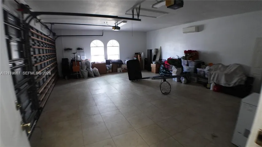 Attached garage featuring tile flooring, arched windows, wall-mounted climate control unit, and extensive built-in wall shelving