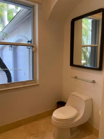Restroom featuring stone-finish flooring, a wall-mounted rectangular mirror with a dark frame, a glass shelf, and a high-profile one-piece toilet