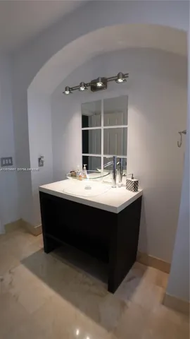 Vanity featuring a dark wood-finish base, neutral countertop, and a clear glass vessel sink with a polished metal faucet
