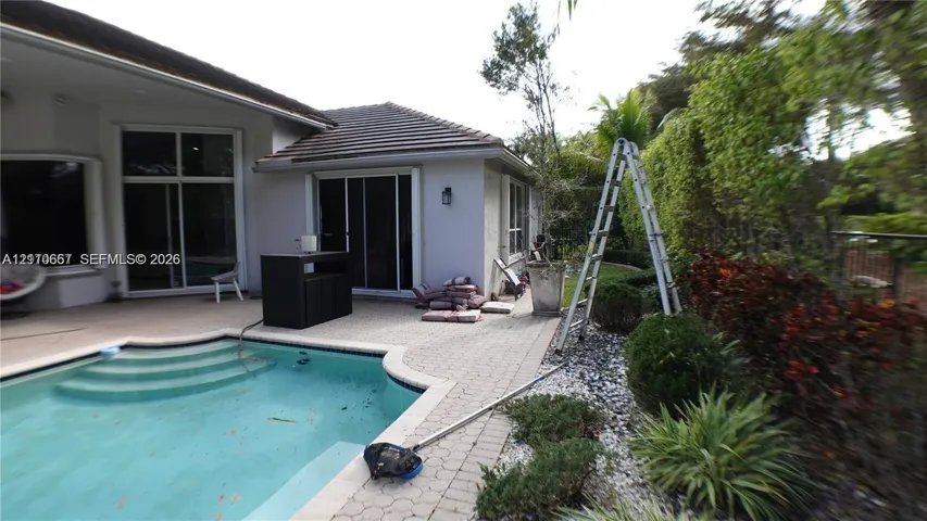 Rear patio featuring concrete paver decking, swimming pool with integrated stairs, and exterior wall-mounted lighting