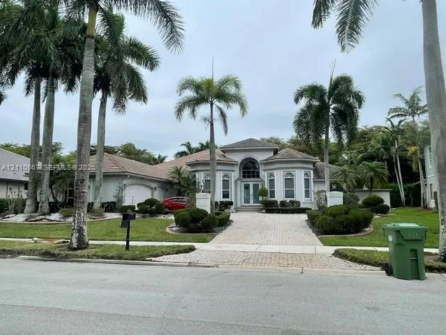 Single-story residence featuring a tiled roof, arched entryway, multi-paned glass double front doors, paved driveway, and mature palm trees