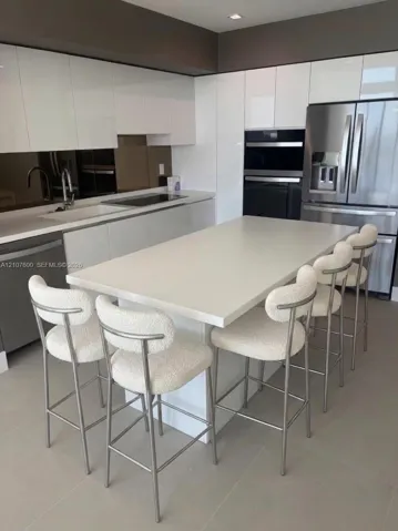 IA - Image Generated - Modern kitchen featuring high-gloss white cabinetry, a center island with a solid surface countertop, stainless steel appliances, and a reflective backsplash