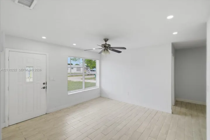 Interior space featuring wood-finish tile flooring, recessed ceiling lighting, a multi-blade ceiling fan, and a six-panel entry door with an integrated glass light