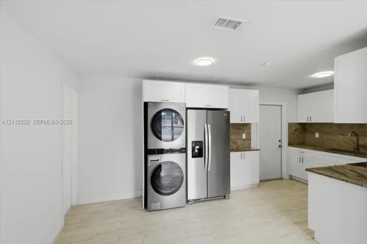 White cabinetry featuring shaker-style doors, stone-finish countertops, stainless steel appliances, and wood-finish flooring