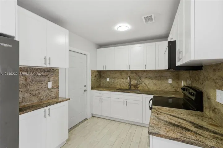 Kitchen featuring white shaker-style cabinetry, stone countertops with matching backsplash, wood-finish flooring, and black built-in appliances