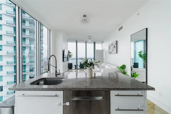 Kitchen island featuring stone countertops, an undermount sink, stainless steel dishwasher, and white cabinetry with metal hardware