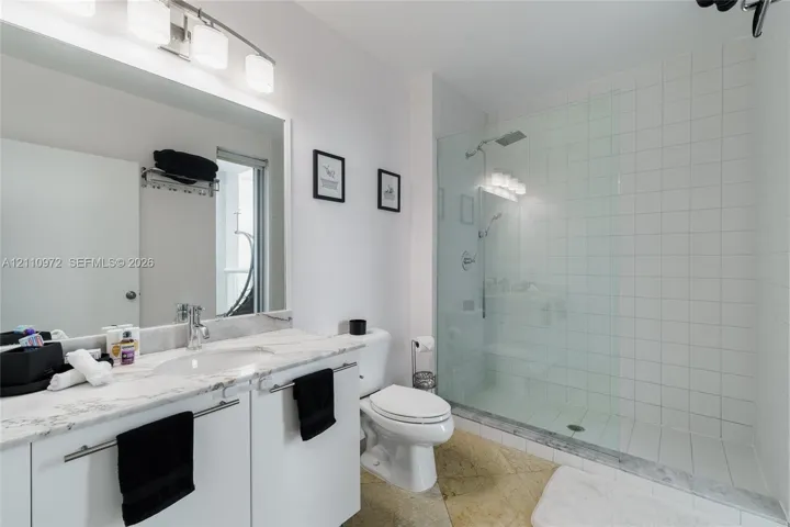 Bathroom featuring a stone-top vanity with an integrated sink, a walk-in shower with a glass partition, wall-mounted lighting, and tile flooring