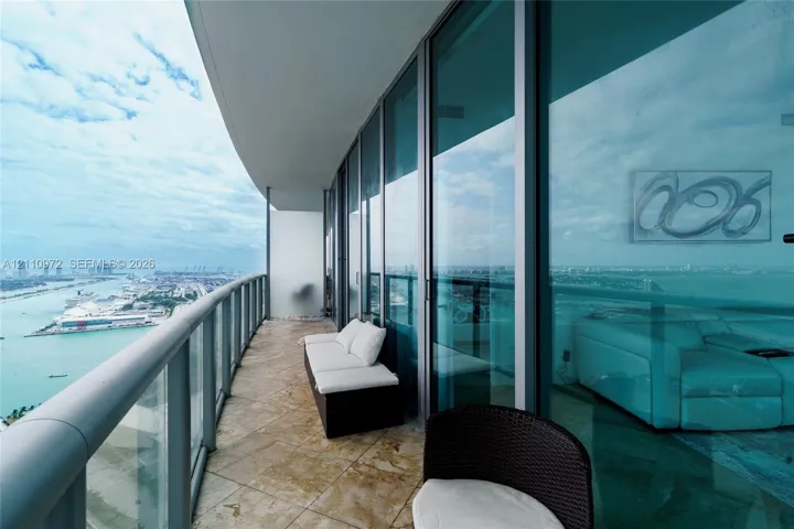 Curved balcony featuring floor-to-ceiling glass paneling, stone tile flooring, and a metal railing