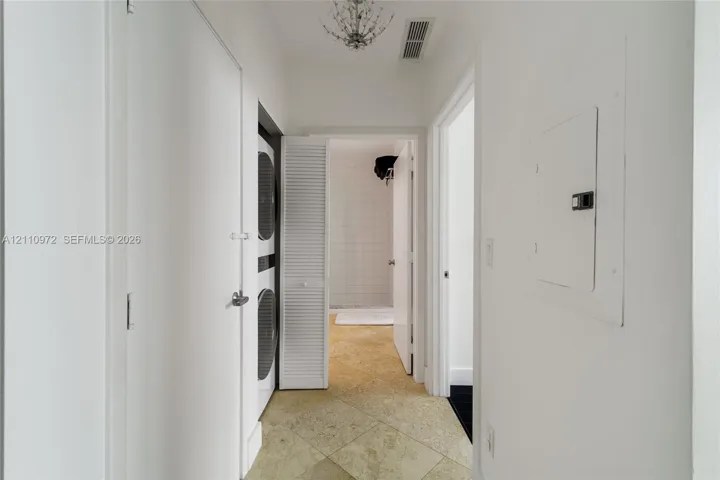 Hallway featuring stone-finish tile flooring, a decorative ceiling-mounted chandelier, and an integrated laundry closet with louvered doors