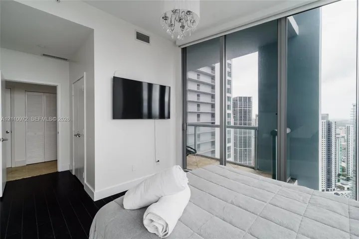 Floor-to-ceiling windows, dark wood-finish flooring, glass-railing balcony, and a decorative chandelier