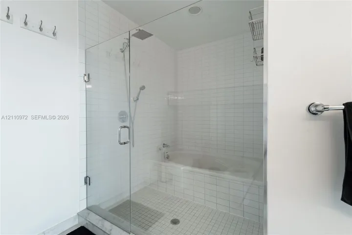 Walk-in shower with frameless glass door, soaking tub, square white wall tiling, rain-style shower head, and chrome fixtures